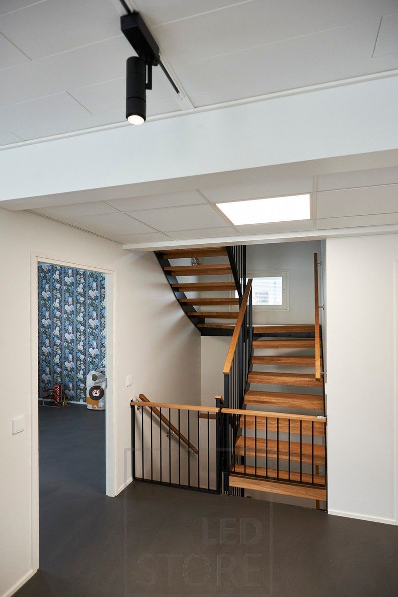 Black led track lights illuminating the space with directional lighting, in front of the stairs a large panel light with wide illumination. Ledstore.fi